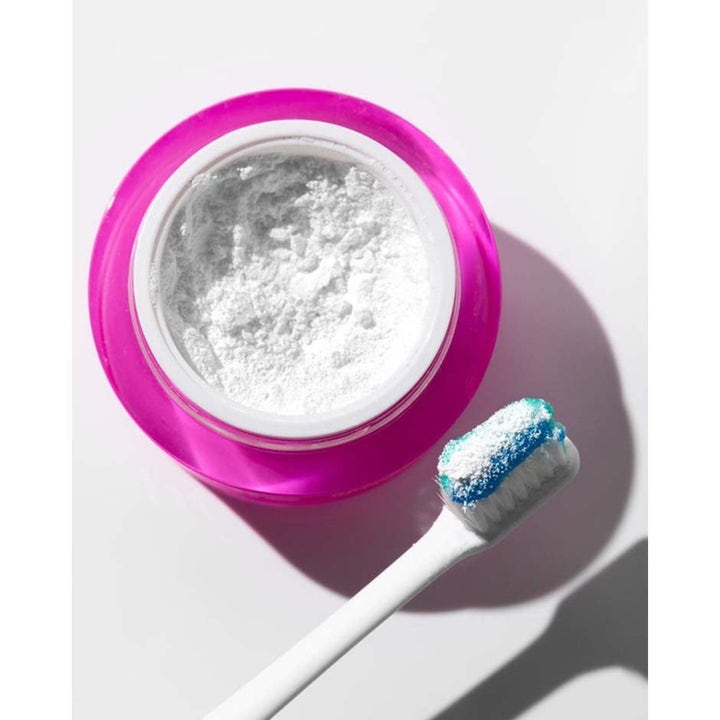 Hismile Whitening Powder 12 g hampaiden valkaisuun on pinkki purkki ja jauheeseen kastettu hammasharja.