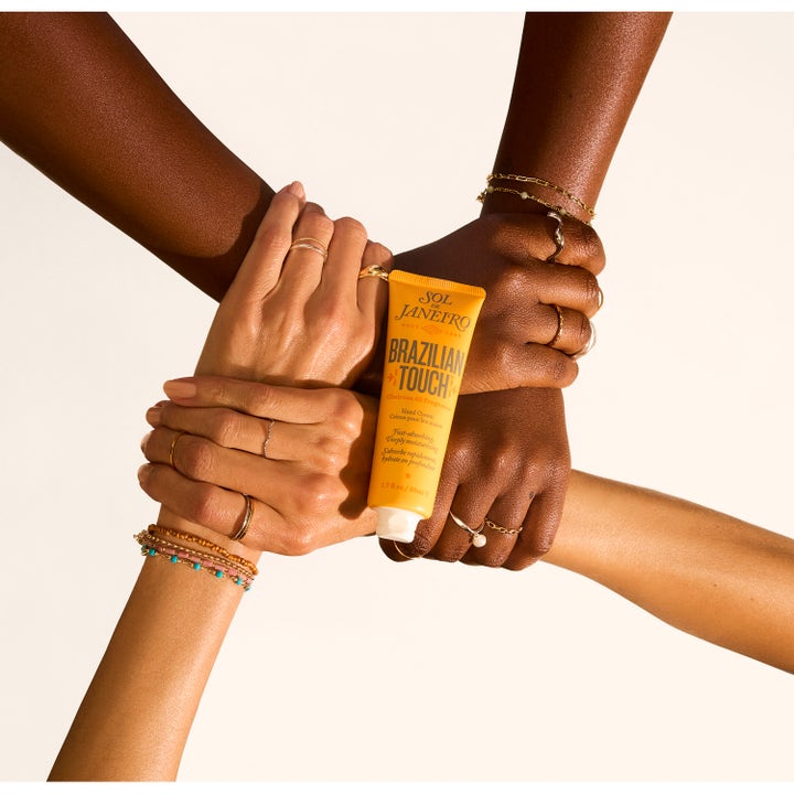 Sol de Janeiro Brazilian Touch 50 ml kosteuttava käsivoide keltaisessa tuubissa useiden käsien pitelemänä.