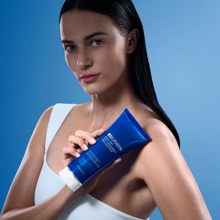 Biotherm Biocorps Body Scrub 200 ml ihoa silottava vartalonkuorinta nainen pitelee sinistä tuubia sinisellä taustalla.