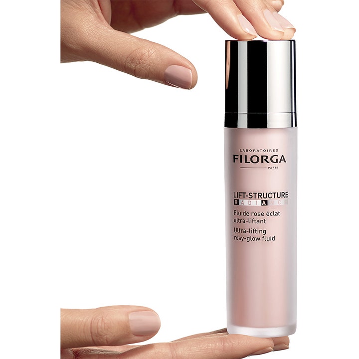 Filorga Lift-Structure Radiance 50 ml heleyttävä päivävoide tyylikkäässä pumppupullossa sormien välissä.