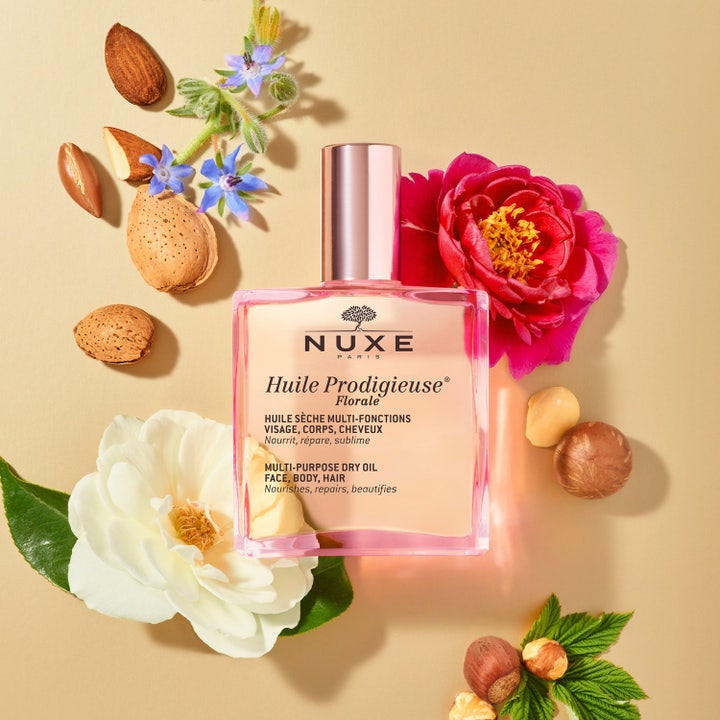 Nuxe Huile Prodigieuse Florale 100 ml ravitseva kuivaöljy lasipullossa ja sarjan muut kukkaiset tuotteet pinkillä taustalla