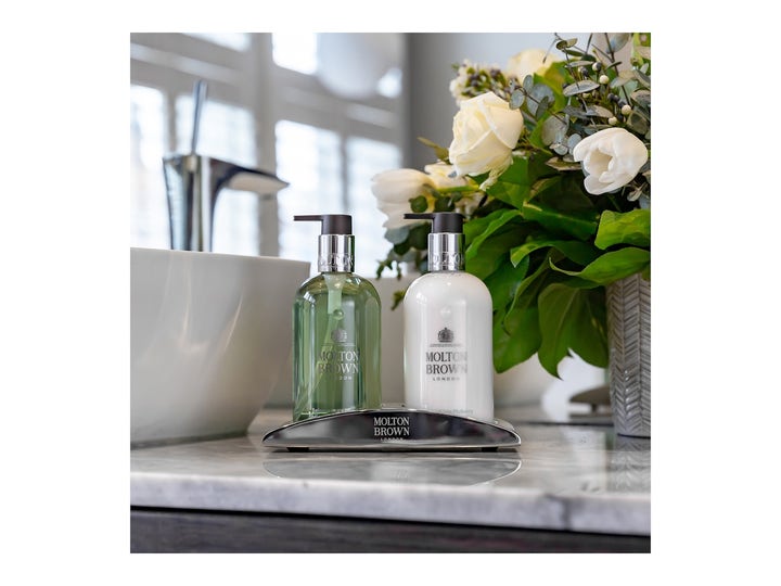 Molton Brown Refined White Mulberry Fine Liquid Hand Wash 300 ml puhdistava käsisaippua hopeisella telineellä kukkien kera.