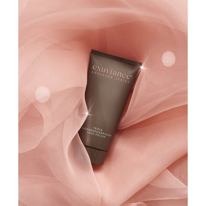 Exuviance Triple Microdermabrasion Face Polish 75 g kuorinta ruskeassa tuubissa vaaleanpunaisen kankaan päällä.