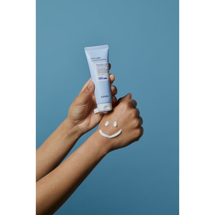 COSRX Ultra-Light Invisible Sunscreen SPF50 50 ml kosteuttava aurinkovoide ja valkoinen voidehymiö käden selällä.