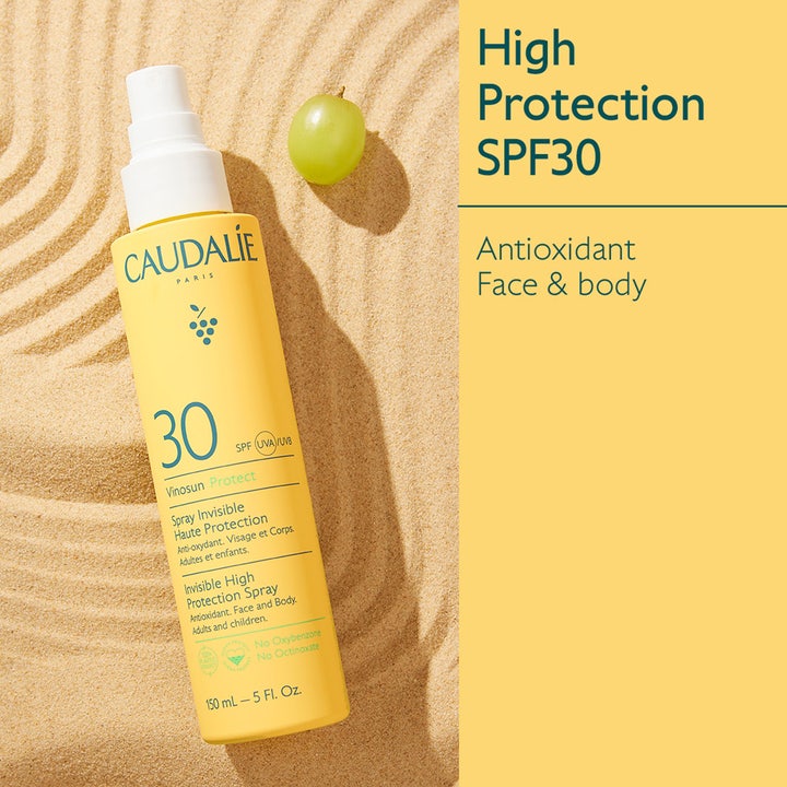 Caudalie Vinosun High Protection Spray SPF30 150 ml aurinkosuojasuihku keltaisessa pullossa hiekalla viinirypäleen kera.
