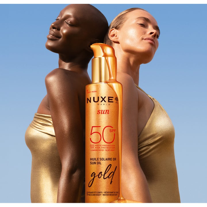 Nuxe Sun Tanning Oil Gold SPF50 150 ml aurinkoöljy antaa hehkua iholle kultaisessa pullossa mallien edessä.