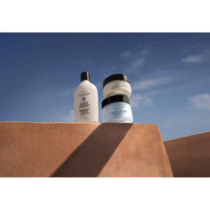 L'Occitane Shea Butter Rich Body Scrub 200 ml vartalokuorinta ja muita voiteita aurinkoisella muurilla.