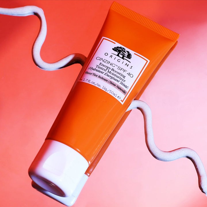 Origins GinZing SPF 40 50 ml sävytetty päivävoide oranssissa tuubissa aaltoilevan voiteen päällä.