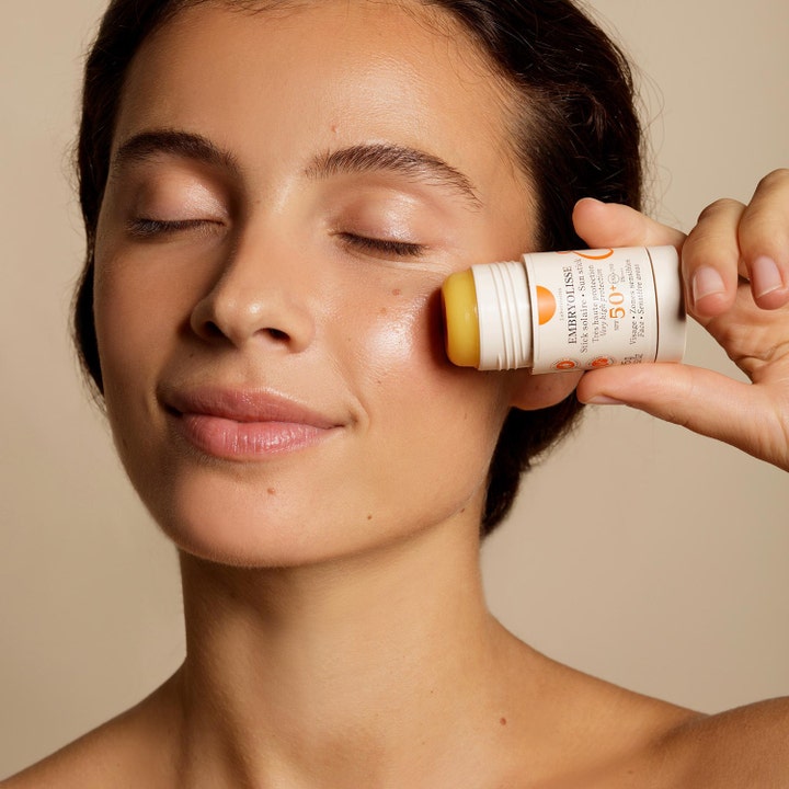Embryolisse Sun Stick SPF50+ 15 g aurinkovoidepuikko nainen levittää keltaista puikkoa poskelleen.