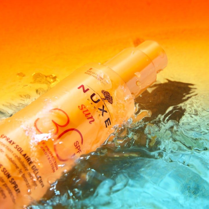 Nuxe Sun Spray SPF30 184 g aurinkosuoja kasvoille oranssissa pullossa veden loiskeiden ympäröimänä.