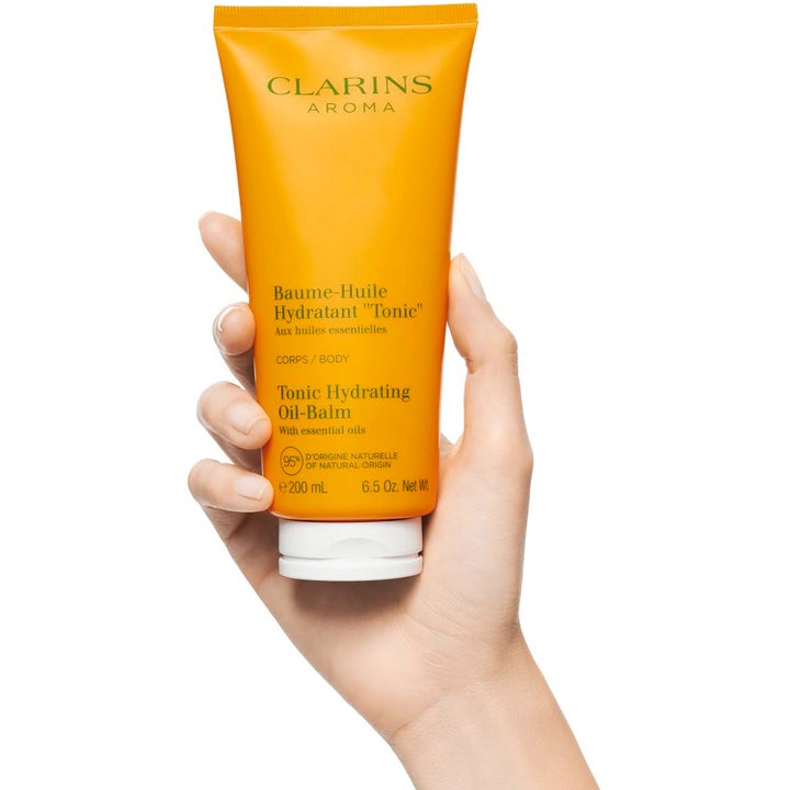 Clarins Tonic Hydrating Oil-Balm 200 ml kosteuttava vartalovoide oranssissa tuubissa kädessä pidettynä.