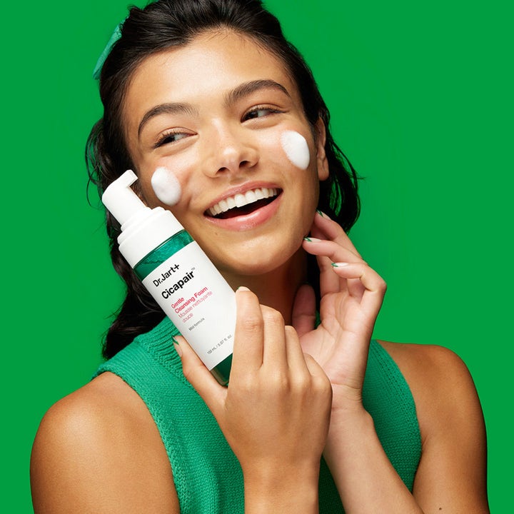 Dr.Jart+ Cicapair Gentle Cleansing Foam 150 ml rauhoittava puhdistusvaahto hymyilevän naisen kasvoilla vihreää vasten.
