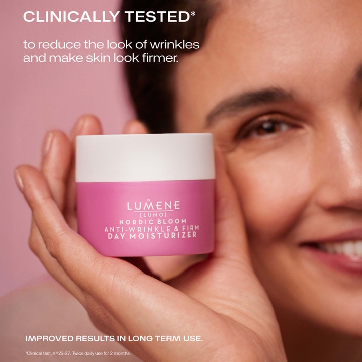 Lumene Nordic Bloom 50 ml kiinteyttävä päivävoide vaaleanpunaisessa purkissa hymyilevän naisen kädessä.