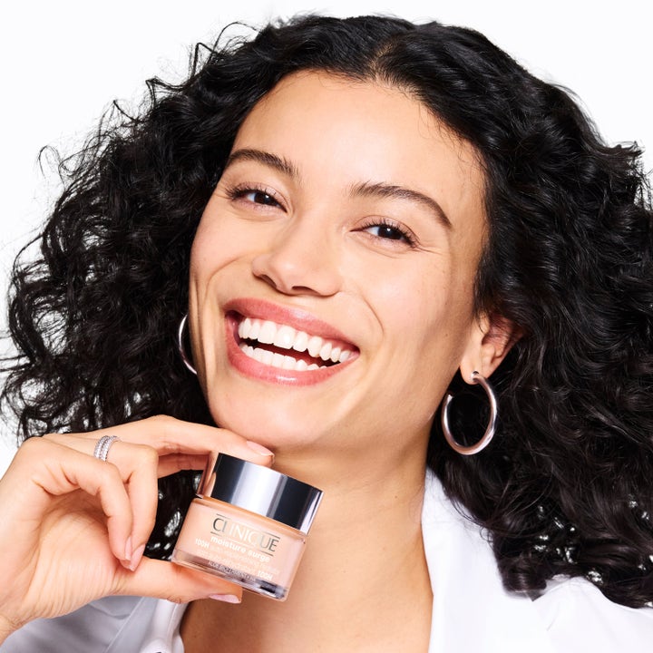 Clinique Moisture Surge 100H syväkosteuttava kasvovoide hopeakorkkisessa purkissa hymyilevän naisen kädessä.