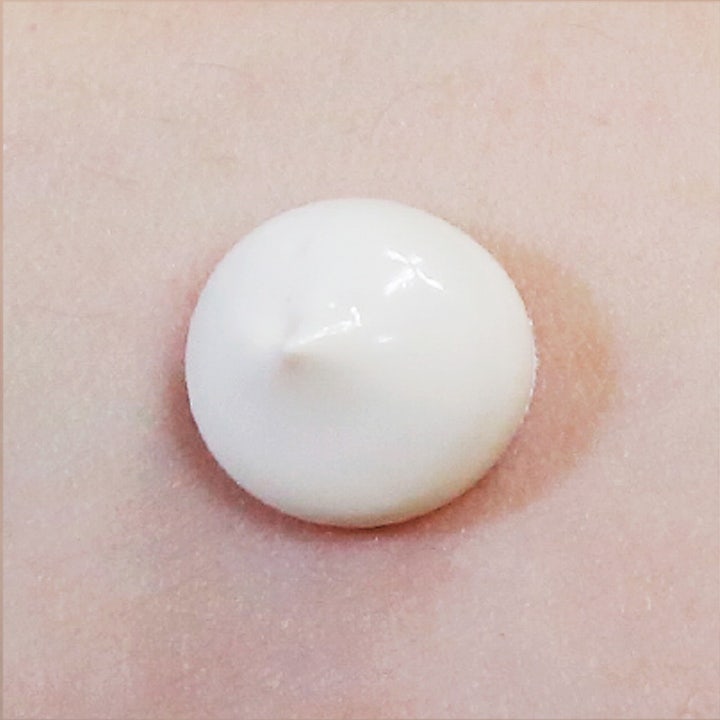 Suntique I'm Tone Up Multi Base 50 ml kirkastava aurinkovoide, jonka pehmeän valkoinen koostumus näkyy iholla.