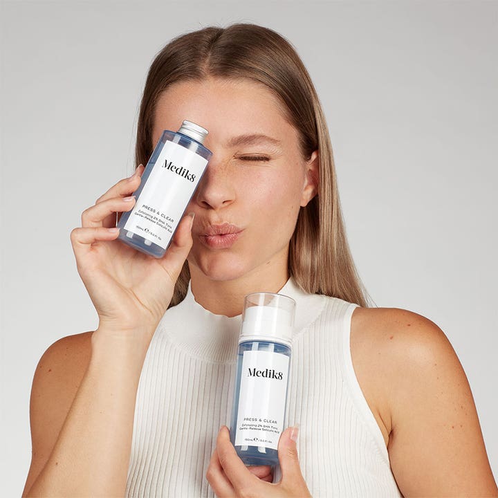 Medik8 Press & Clear 150 ml kuoriva BHA-kasvovesi nainen pitelee pumppupulloa ja täyttöpakkausta