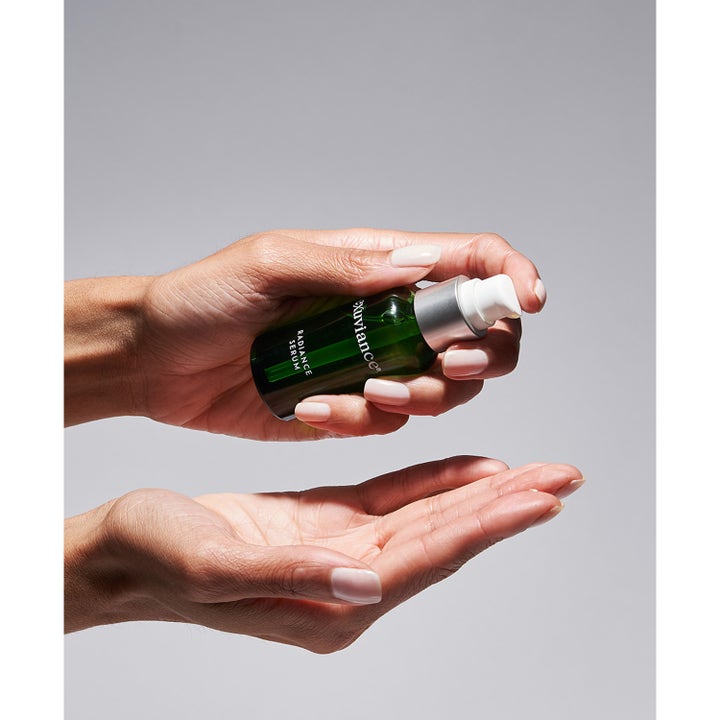 Exuviance Radiance Serum 30 ml kirkastava seerumi vihreässä pumppupullossa annosteltuna kämmenelle.