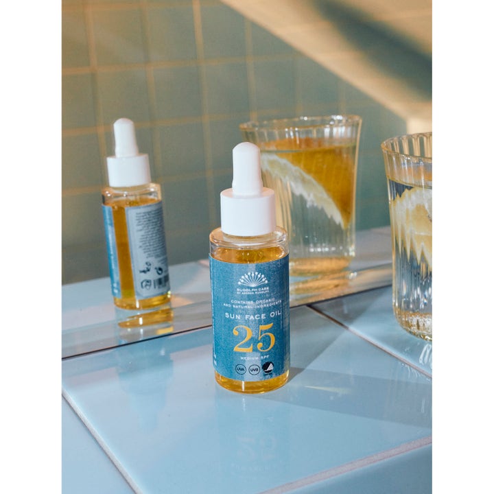 Rudolph Care Sun Face Oil SPF25 50 ml suojaava kasvoöljy lasisessa pipettipullossa sinisellä etiketillä peilin edessä.