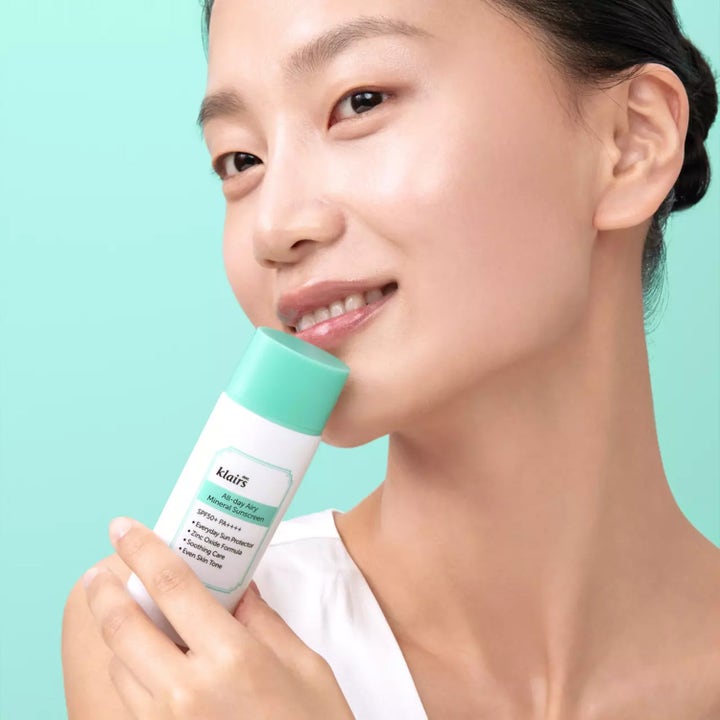 Klairs All-day Airy Mineral Sunscreen 60 g rauhoittava aurinkovoide SPF 50+ naisen pitelemässä vihreäkorkkisessa tuubissa.