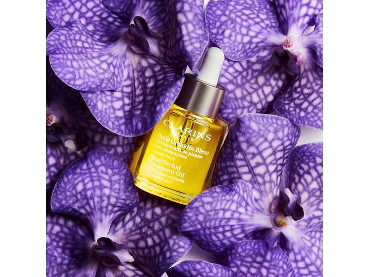 Clarins Blue Orchid Face Treatment Oil 30 ml kosteuttava kasvoöljy pipettipullossa violettien orkideoiden keskellä.