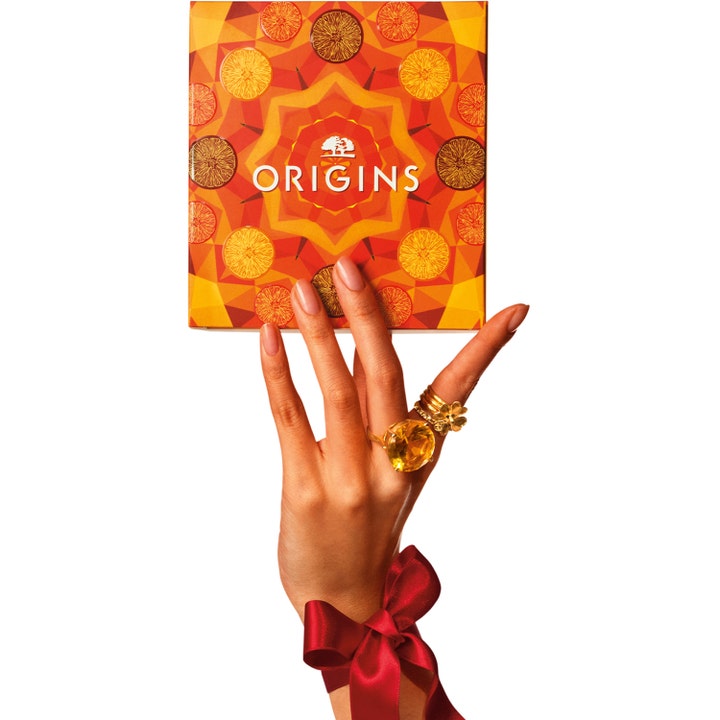 Origins Ginzing Glowing Essentials Set heleyttävä ihonhoitosetti oranssissa rasiassa jota pitelee käsi rusetilla