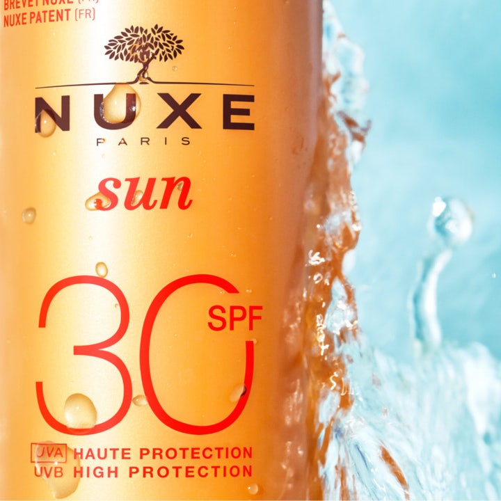Nuxe Sun Spray SPF30 184 g aurinkosuoja, jonka täyteläinen valkoinen voidekoostumus valuu oranssin pullon päällä.