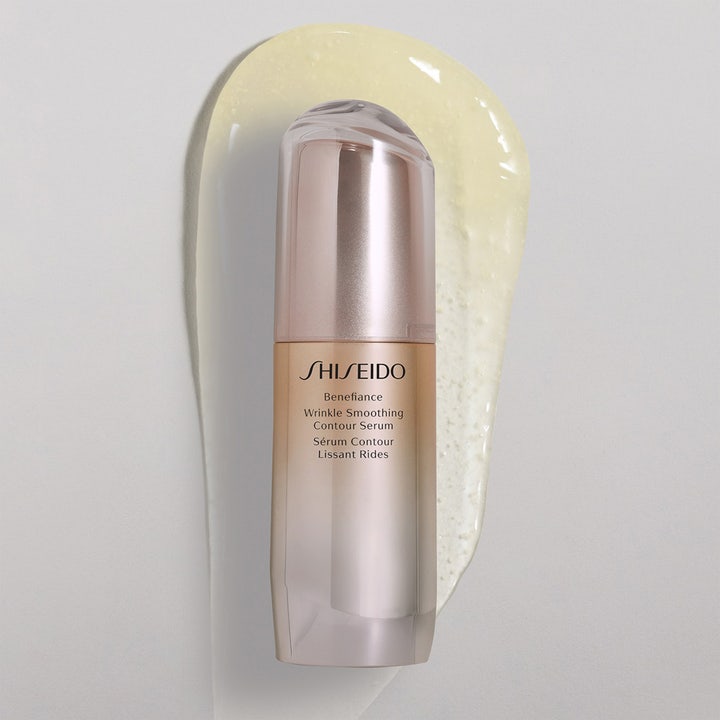 Shiseido Benefiance Wrinkle Smoothing Serum 30 ml silottaa ryppyjä rosekultaisessa pullossa keltaisen tekstuurin päällä.