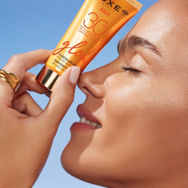 Nuxe Sun-Kissed Fluid Spf 30 40 ml hehkua tuova kasvoaurinkovoide oranssissa tuubissa naisen hehkuvalla iholla