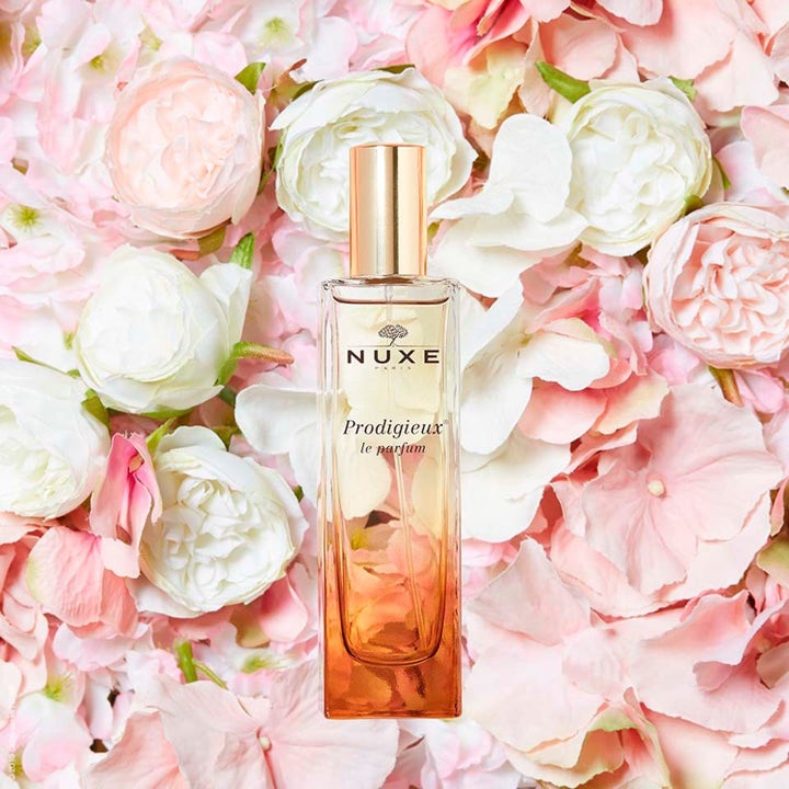 Nuxe Prodigieux le parfum 50 ml tuoksuva Eau de Parfum lasipullossa vaaleanpunaisten kukkien ympäröimänä.