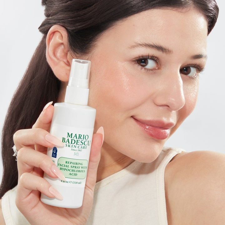 Mario Badescu Repairing Facial Spray 118 ml rauhoittava kasvosuihke nainen pitelee pulloa hehkuvilla kasvoilla.
