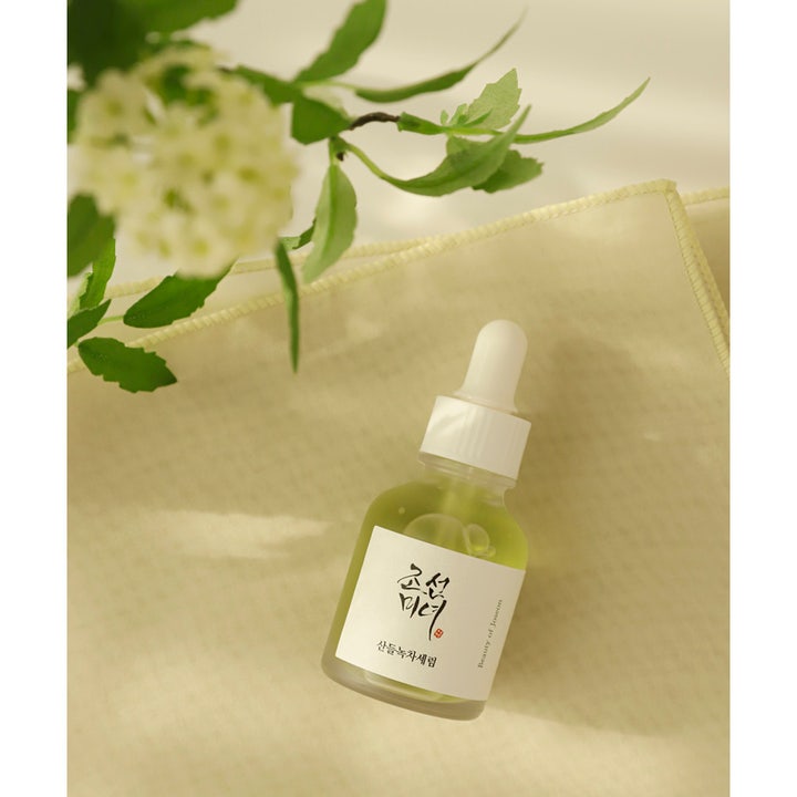 Beauty of Joseon Calming Serum 30 ml rauhoittava vihreä teeseerumi lasisessa pipettipullossa kukkien vieressä.