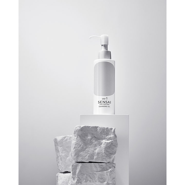 Sensai Silky Purifying Cleansing Oil Step 1 150 ml puhdistusöljy valkoisessa pullossa kivien päällä.