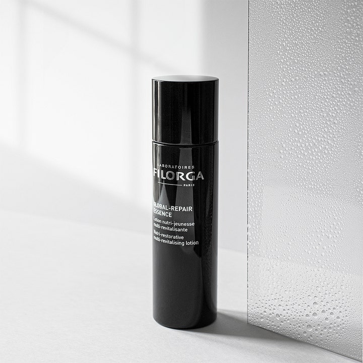 Filorga Global-Repair Essence 150 ml ravitseva hoitoneste mustassa pullossa huurteisen lasin vieressä.