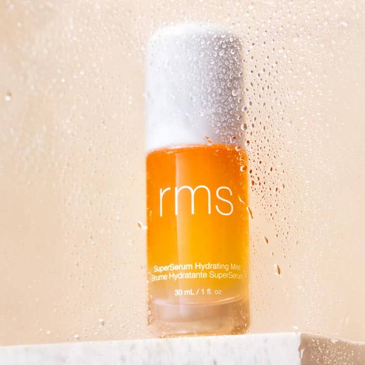 RMS Beauty SuperSerum Hydrating Mist 30 ml kosteuttava kasvosuihke oranssissa pullossa vesipisaroiden takana
