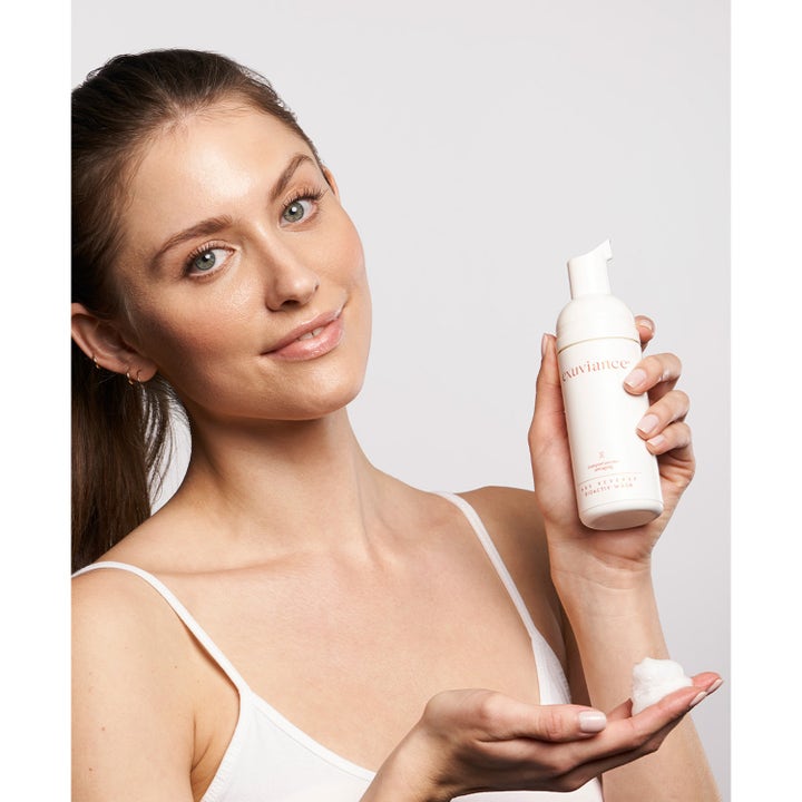 Exuviance Age Reverse BioActiv Wash 125 ml uudistava puhdistusvaahto valkoisessa pumppupullossa naisen kädessä