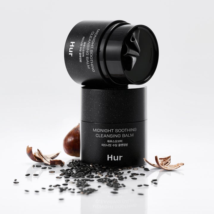 House of Hur Midnight Soothing Cleansing Balm 50 ml rauhoittava puhdistusvoide mustassa purkissa siementen ympäröimänä.