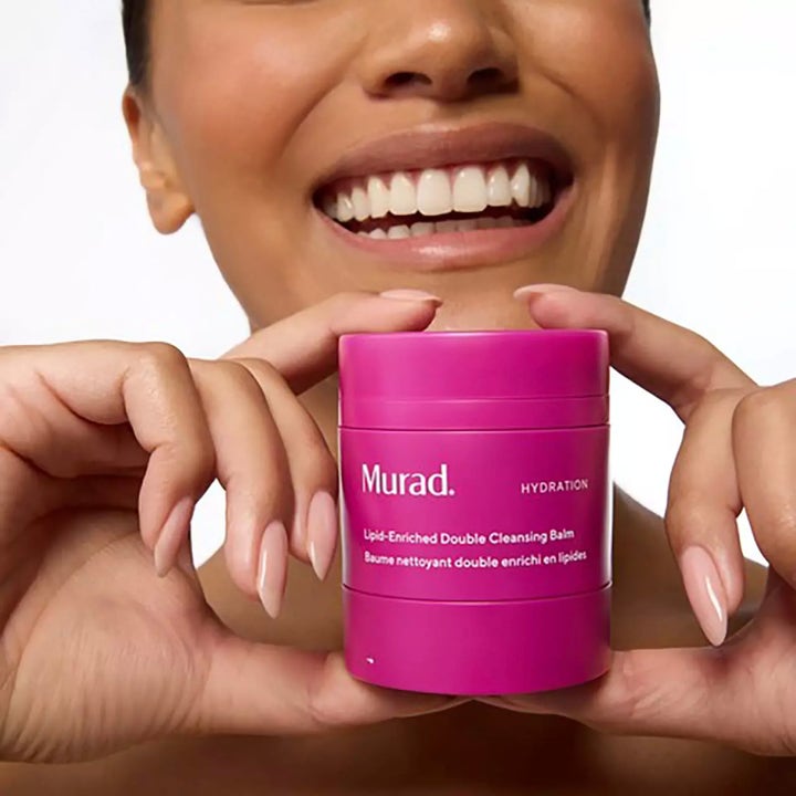 Murad Lipid-Enriched Double Cleansing Balm 50 ml kosteuttava puhdistusvoide pinkissä purkissa hymyilevän henkilön käsissä