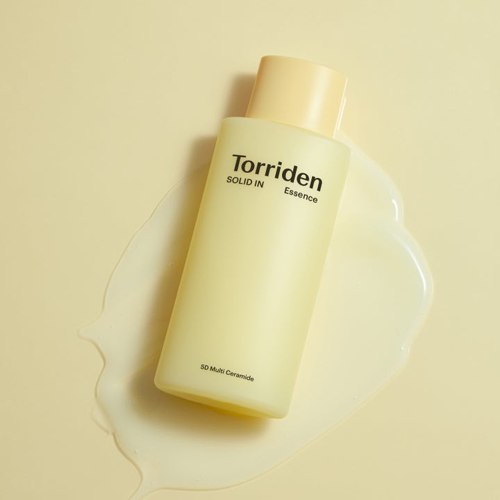 Torriden SOLID-IN All Day Essence 100 ml kosteuttava hoitoneste keltaisessa pullossa nestemäisen tekstuurin päällä