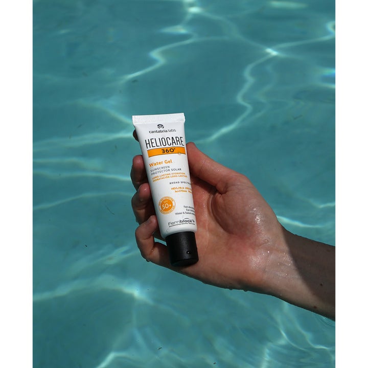 Heliocare Watergel SPF 50+ 50 ml kosteuttava aurinkovoide kädessä turkoosin uima-altaan yllä