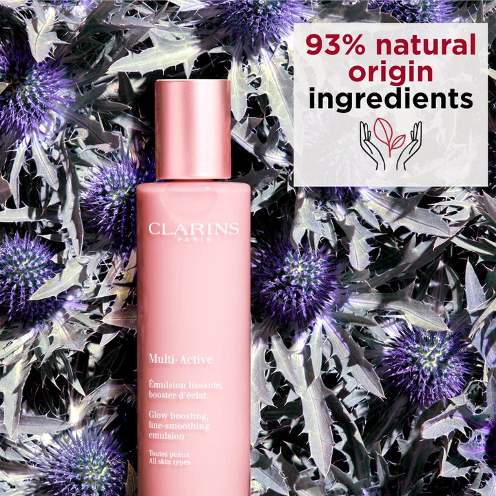 Clarins Multi-Active 100 ml heleyttävä emulsio pinkissä pullossa violettien kukkien päällä, 93 % luonnollisia ainesosia.