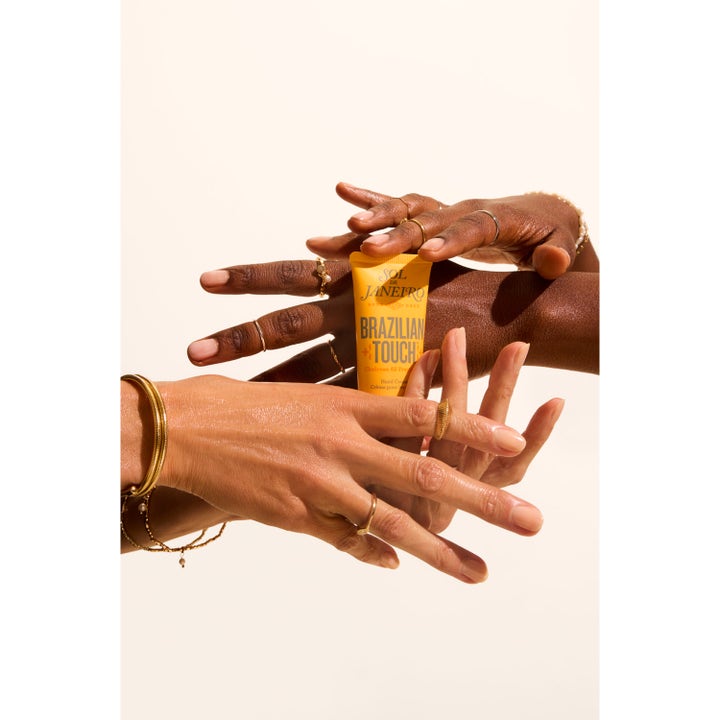 Sol de Janeiro Brazilian Touch Hand Cream 50 ml kosteuttava käsivoide keltaisessa tuubissa koruja kantavien käsien välissä