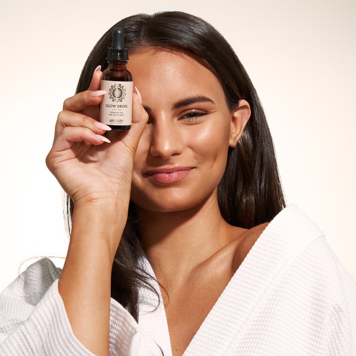 Bronza Glow Drops 30 ml itseruskettavat tipat joita nainen pitelee kasvojensa edessä