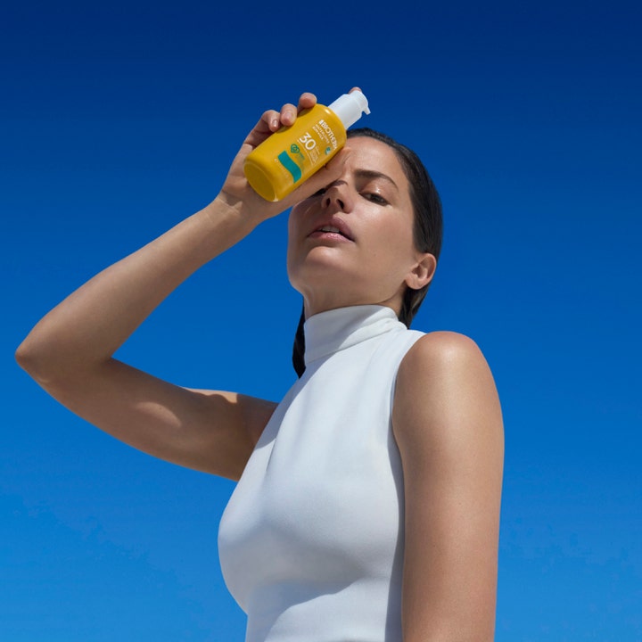 Biotherm Waterlover Sun Milk 200 ml kosteuttava aurinkovoide SPF 30 nainen pitelee keltaista pulloa sinistä taivasta vasten