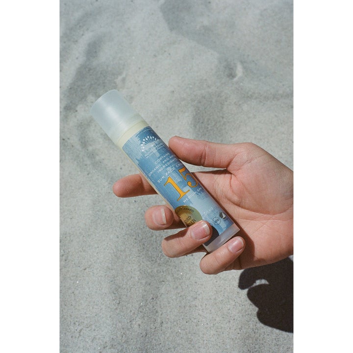 Rudolph Care Sun Face Cream 50 ml SPF15 suojaava kasvovoide kädessä hiekalla sinisessä pumppupullossa.