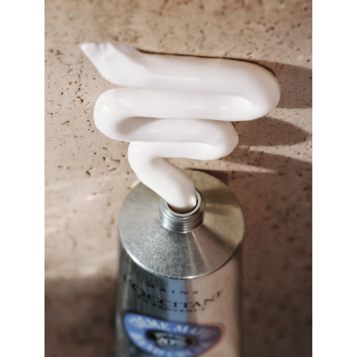 L'Occitane en Provence Shea Butter 150 ml käsivoide ja hopeisesta tuubista pursuava täyteläinen valkoinen voide