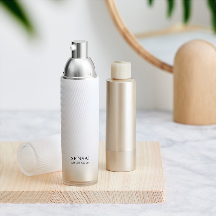 Sensai Essence Day Veil 40 ml suojaava päivävoide valkoisessa pumppupullossa ja täyttöpakkaus puualustalla