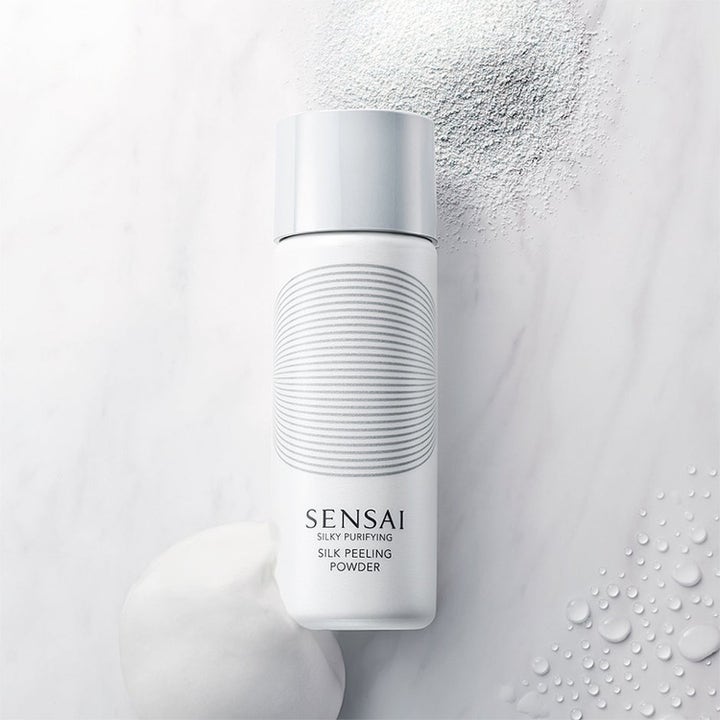 Sensai Silky Purifying Silk Peeling Powder syväpuhdistava kuorinta, hienoa jauhetta ja pehmeää vaahtoa marmorilla.