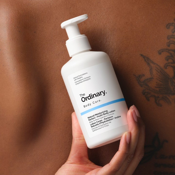 The Ordinary NMF + Inulin Body Lotion 240 ml kosteuttava vartalovoide valkoisessa pumppupullossa kädessä ihoa vasten