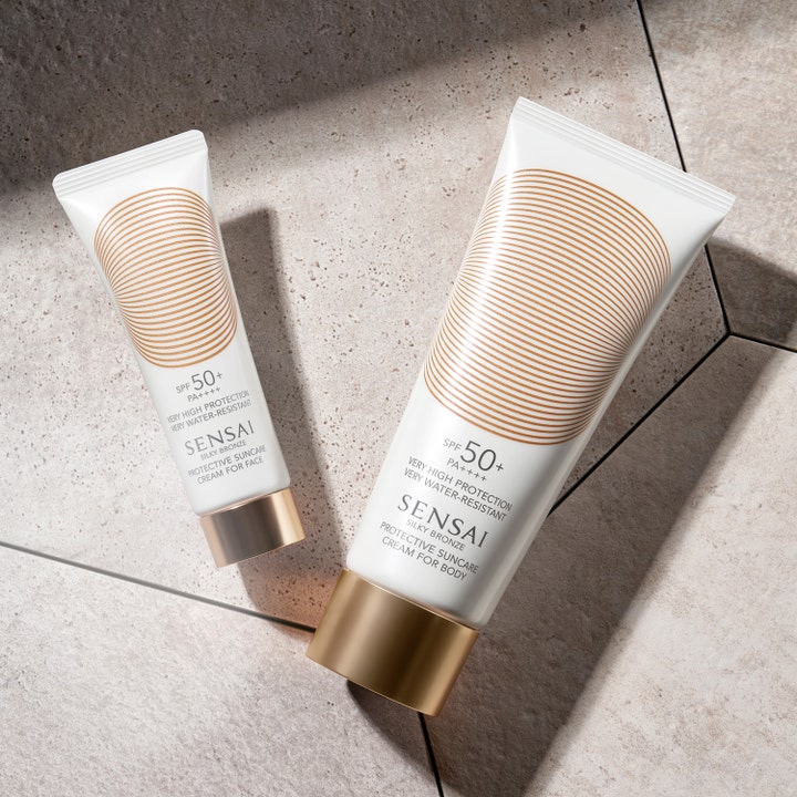 Sensai Silky Bronze Protective Cream Face SPF50+ 50 ml suojaava aurinkovoide valkoisessa tuubissa kivipinnalla.