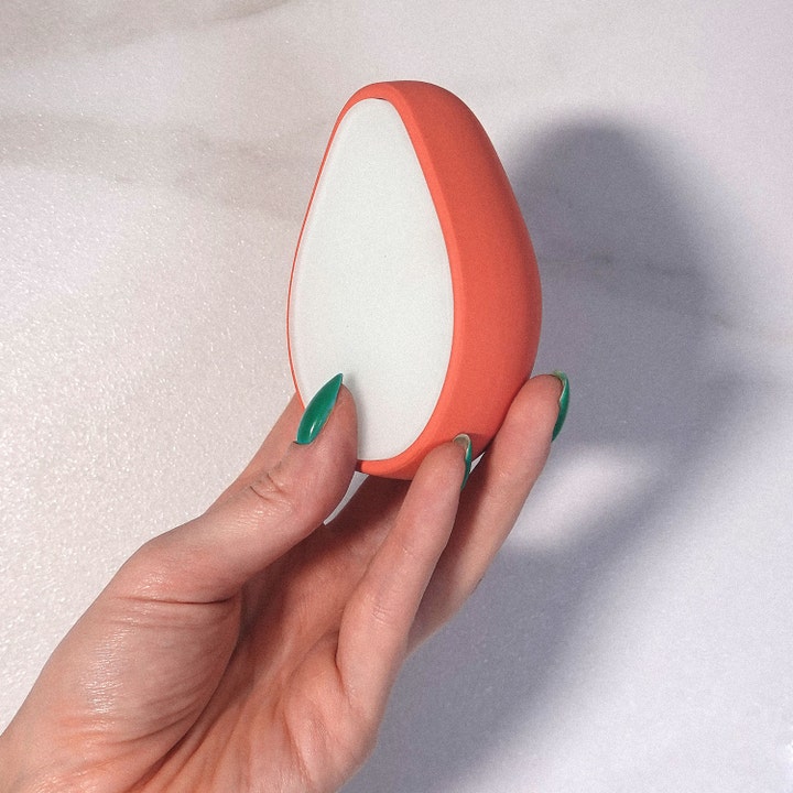 ANSWR Exfoliating Hair Removal Drop 1 kpl kuoriva karvanpoistoväline on oranssi pisaranmuotoinen työkalu kädessä.